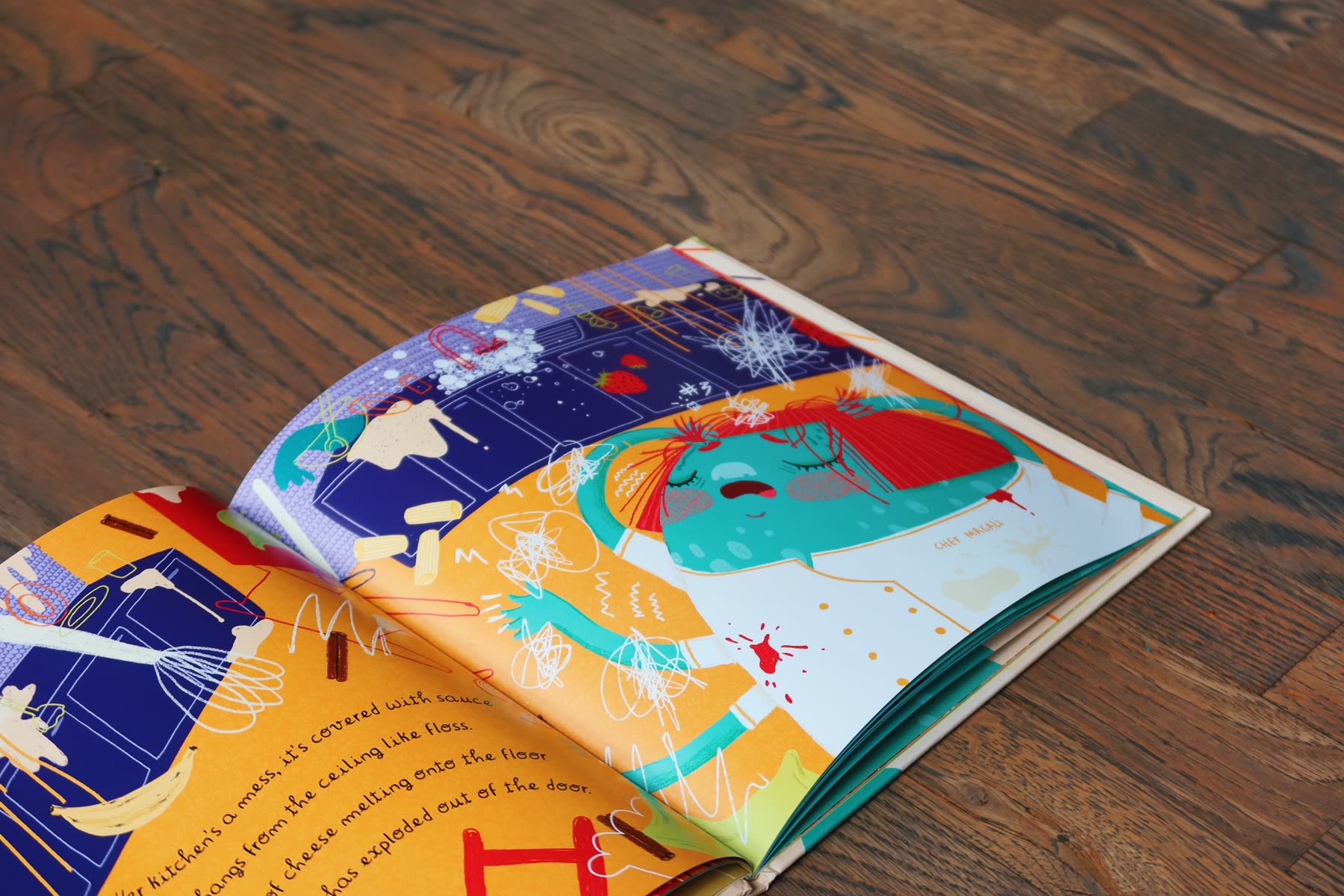 The book lying open on a wooden floor at a full-colour illustrated spread