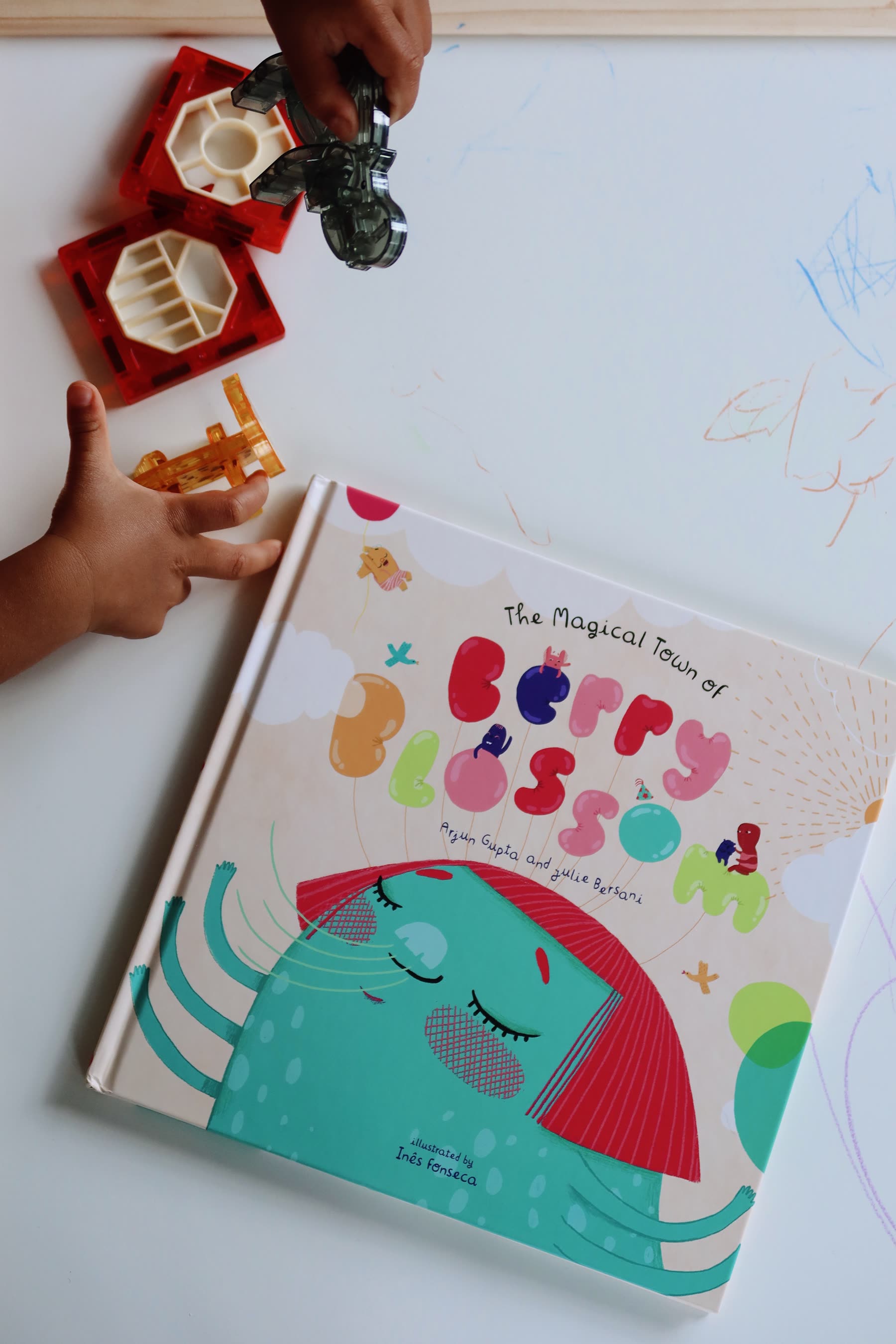 A child's hands reaching for the book on a white table beside toys