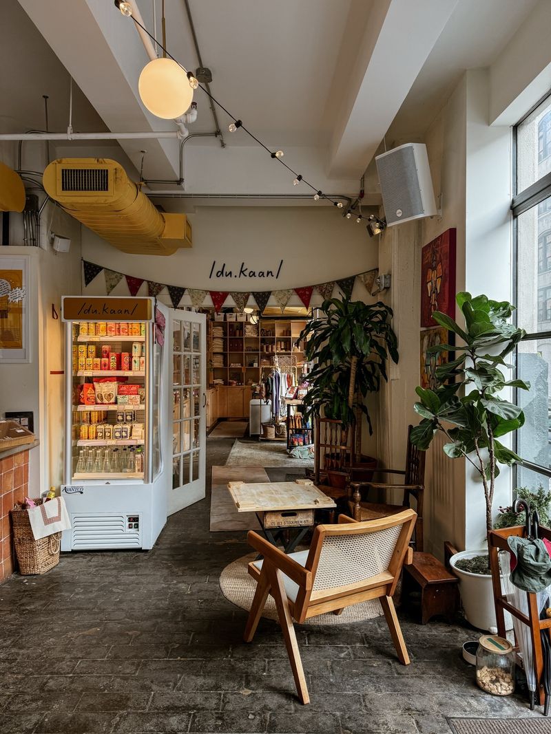Inside Fontainhas in Dumbo: a stocked yellow fridge and shelves under the du.kaan sign, with a cane chair and potted plants on the stone floor